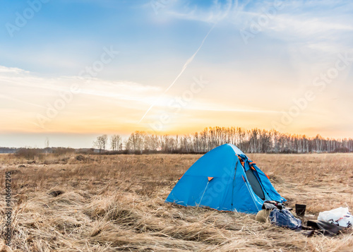 Blue tent in the field at sunset in early spring field
