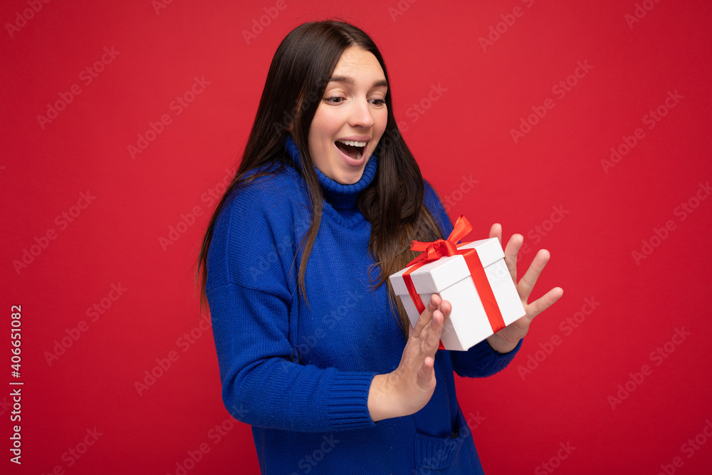 Photo shot of pretty positive surprised young brunet woman isolated over colourful background wall wearing trendy outfit look holding gift box and looking at present box with red ribbon Photo shot of pretty positive surprised young brunet woman isolated over colourful background wall wearing trendy outfit look holding gift box and looking at present box with red ribbon