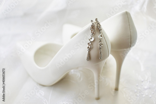graceful earrings of the bride on the white leather shoes. wedding accessories. close-up, macro