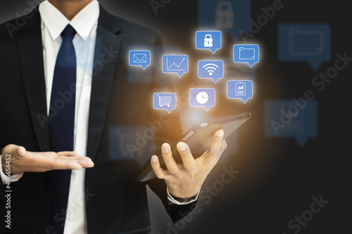 Businessman wearing black suit with icons digital on screen digital tablet in back background smart connection network information, concept of technology.