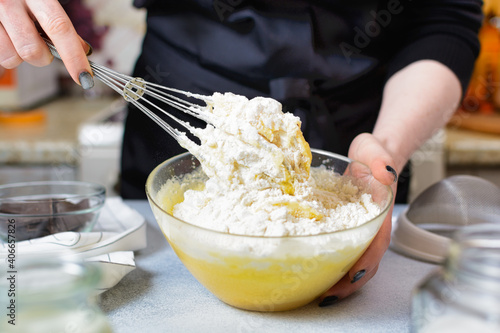 the chef prepares flour dough with a metal whisk in a glass bowl