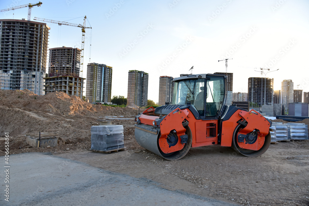 Paving roller machine during road work at construction site for paving works. Asphalt paver Road roller for Screeding the sand and road concreting. Tower cranes in action under buildings
