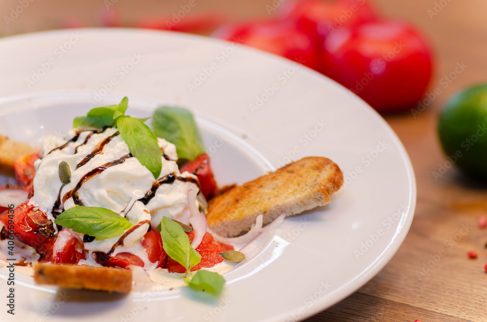 Salad with goat cheese, tomatoes, baguette on a white plate. Close-up