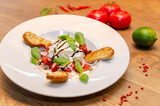 Salad with goat cheese, tomatoes, baguette on a white plate. Close-up