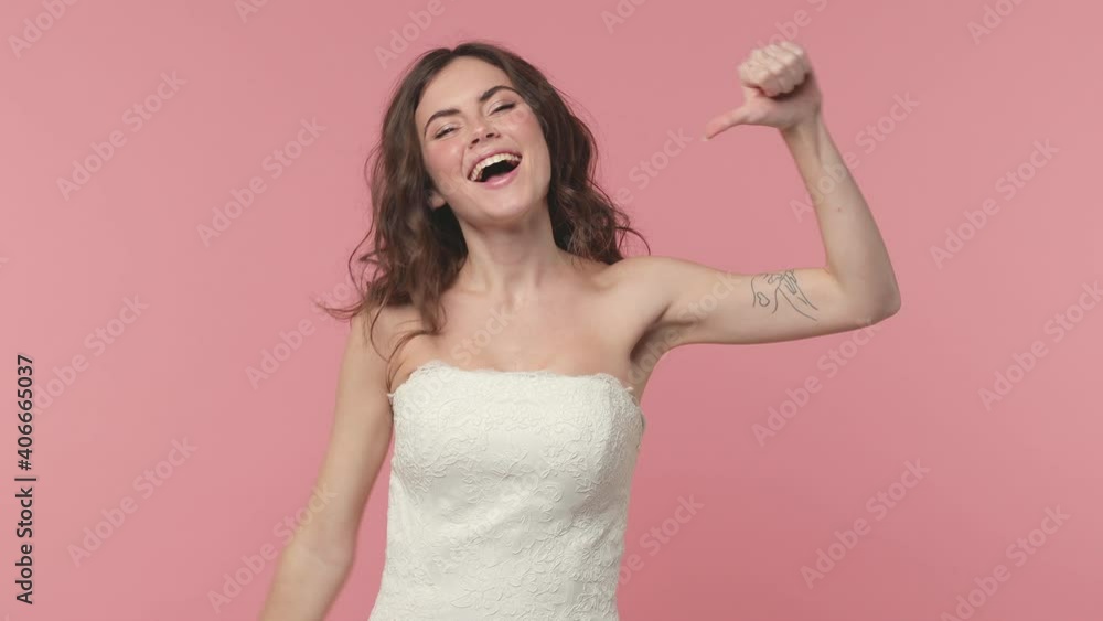 Excited cheerful bride young brunette woman 20s years old in beautiful white wedding dress posing isolated on pink pastel color background studio. Wedding concept. Pointing thumb on herself blinking Excited cheerful bride young brunette woman 20s years old in beautiful white wedding dress posing isolated on pink pastel color background studio. Wedding concept. Pointing thumb on herself blinking