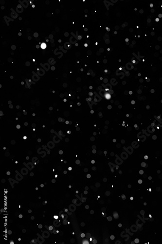 Bokeh of white snow on a black background. Falling snowflakes on night sky background, isolated for post production and overlay in graphic editor.