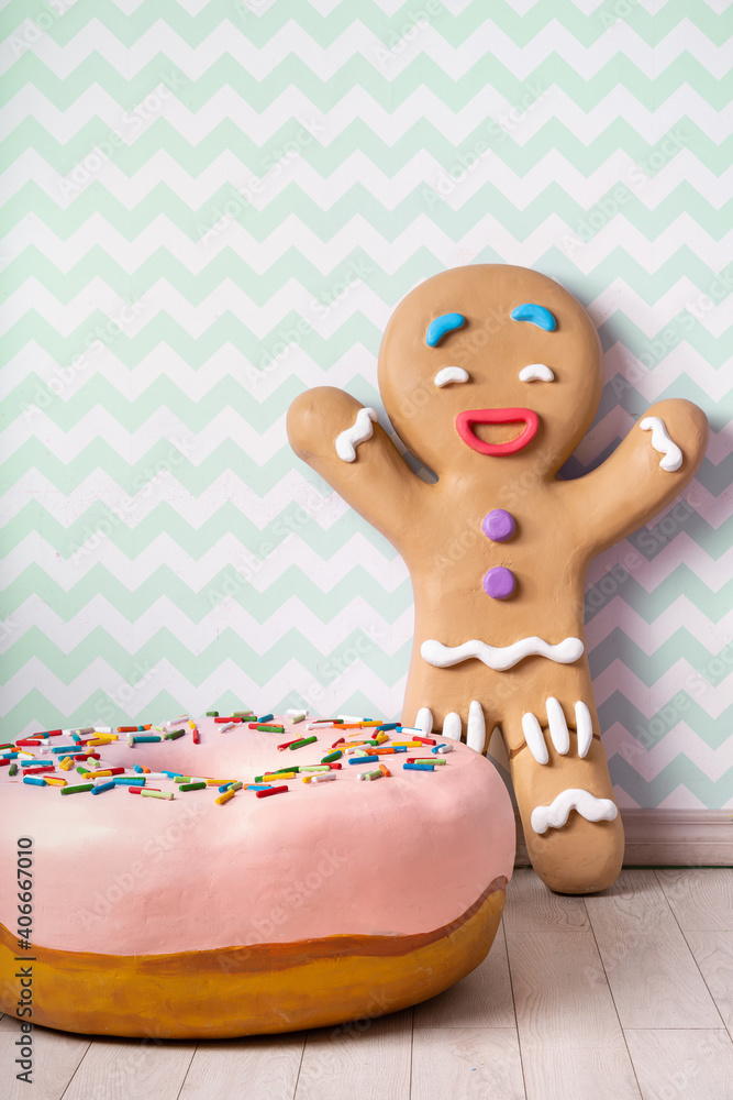 Obraz premium A large glazed donut and a giant gingerbread man against a striped green wall.