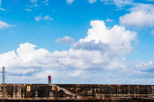 A single man stands on the harbour walls looking outwards towards the open sea and the vast expanse of a lovely sky.