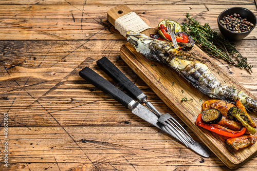 Grilled whole icefish with vegetables. Wooden background. Top view. Copy space