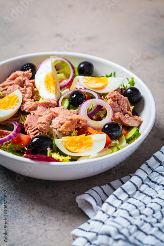 Tuna salad with egg, olives and vegetables in white bowl, dark background. Diet food concept.