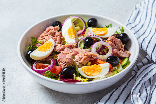 Tuna salad with egg, olives and vegetables in white bowl, white background. Diet food concept. photo