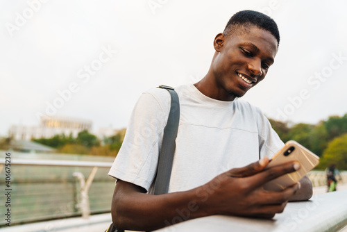 Happy african american guy using mobile phone on urban bridge