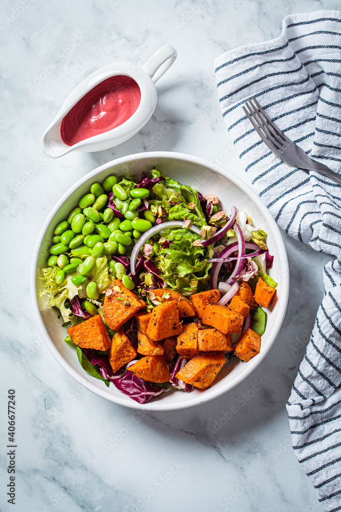 Vegan salad bowl with baked sweet potato, edamame beans, nuts and pink beetroot dressing. Vegan food concept.