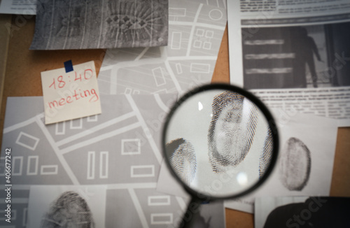 Looking through magnifying glass at fingerprints on detective board, closeup photo