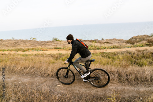 Handsome unshaven guy in sunglasses riding his bicycle at coast