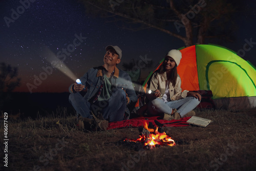Couple with flashlights near bonfire at night. Camping season