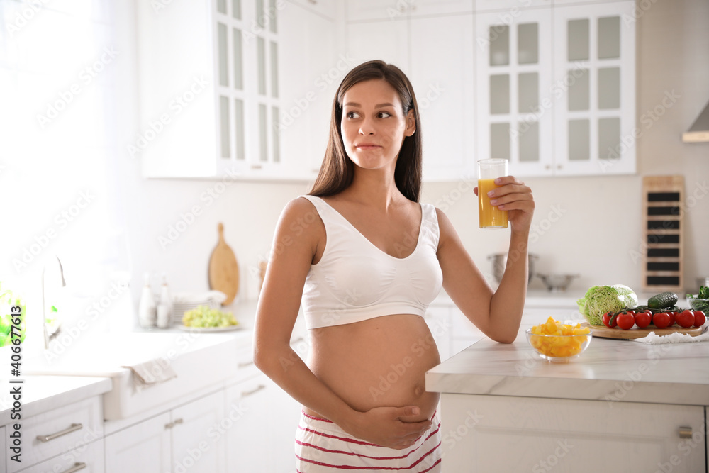 Young pregnant woman with glass of juice in kitchen. Taking care of baby health Young pregnant woman with glass of juice in kitchen. Taking care of baby health