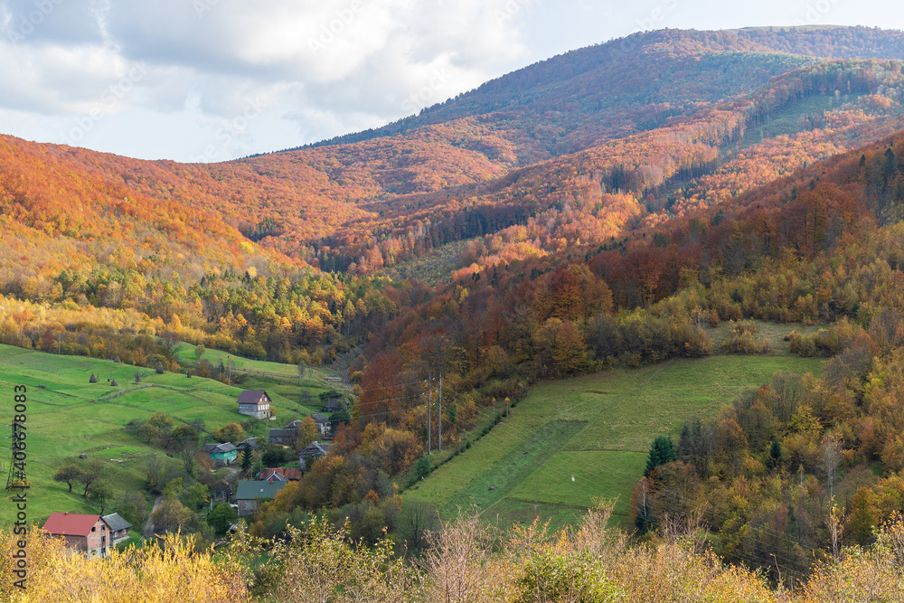 Magnificent panorama of a picturesque mountain village in autumn. Autumn mountain landscape in the Ukrainian Carpathians - yellow and red trees combined with green needles.