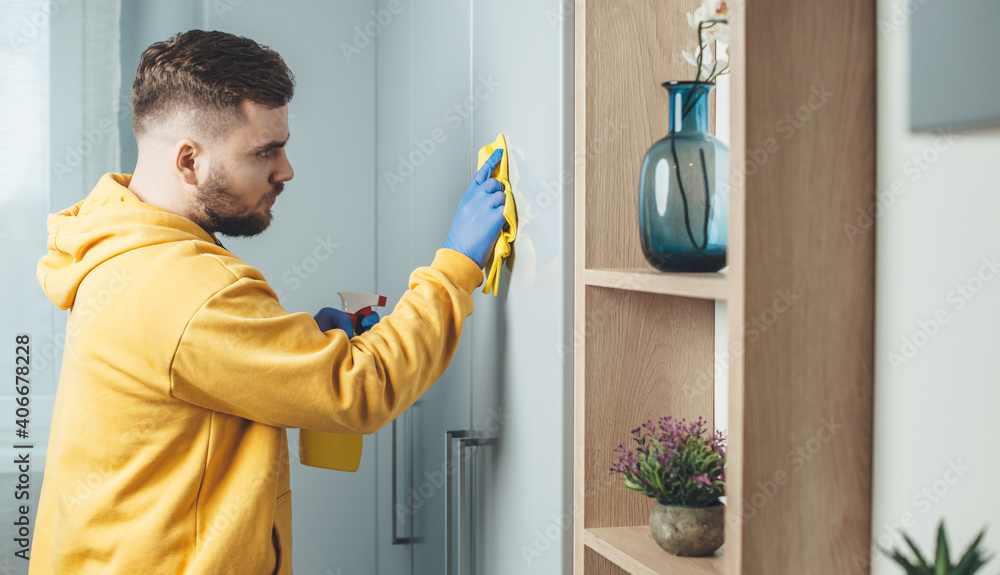 Caucasian man wearing blue gloves is cleaning the house using wipe and disinfecting spray