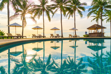 Beautiful luxury umbrella and chair around outdoor swimming pool in hotel and resort with coconut palm tree on sunset  or sunrise sky