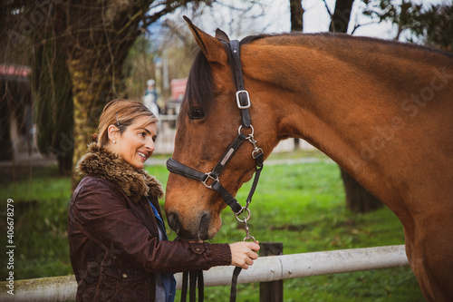 Short-haired woman in a brown jacket smiling and looking closely into her horse's eyes