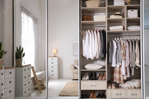 Wardrobe closet with different stylish clothes, shoes and home stuff in room photo