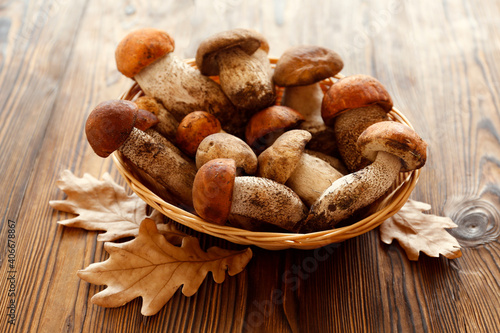 Bunch of porcini mushrooms in small wicker basket on wood textured table. Copy space for text, close up, top view, background.