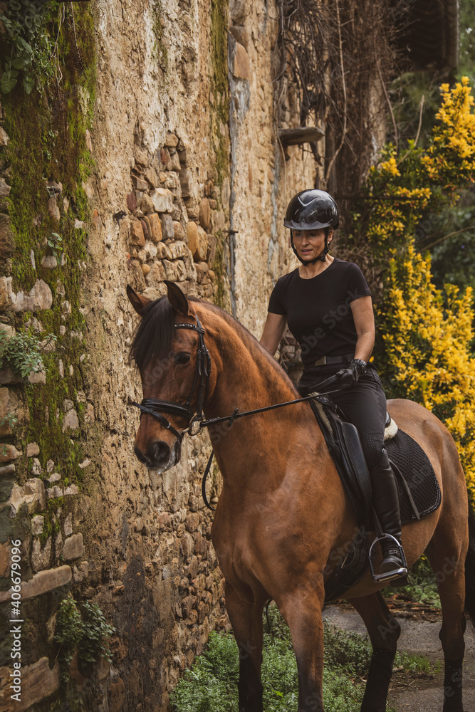 woman riding her brown horse with black mane dressed in black with a helmet woman riding her brown horse with black mane dressed in black with a helmet