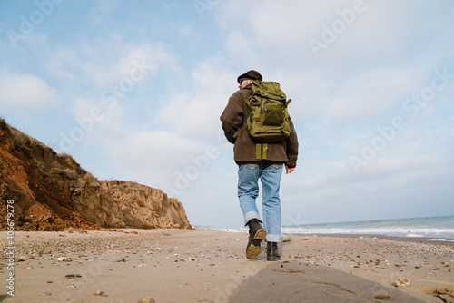 Cropped photo of man with backpack walking on beach