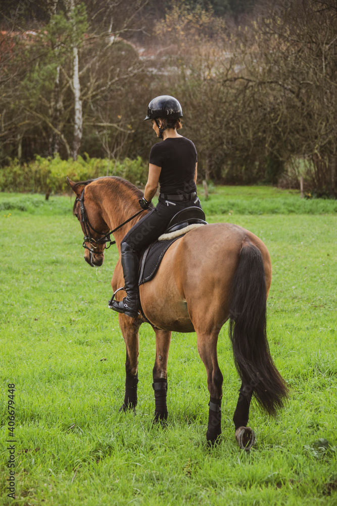 woman riding her brown horse with black mane dressed in black with a helmet woman riding her brown horse with black mane dressed in black with a helmet