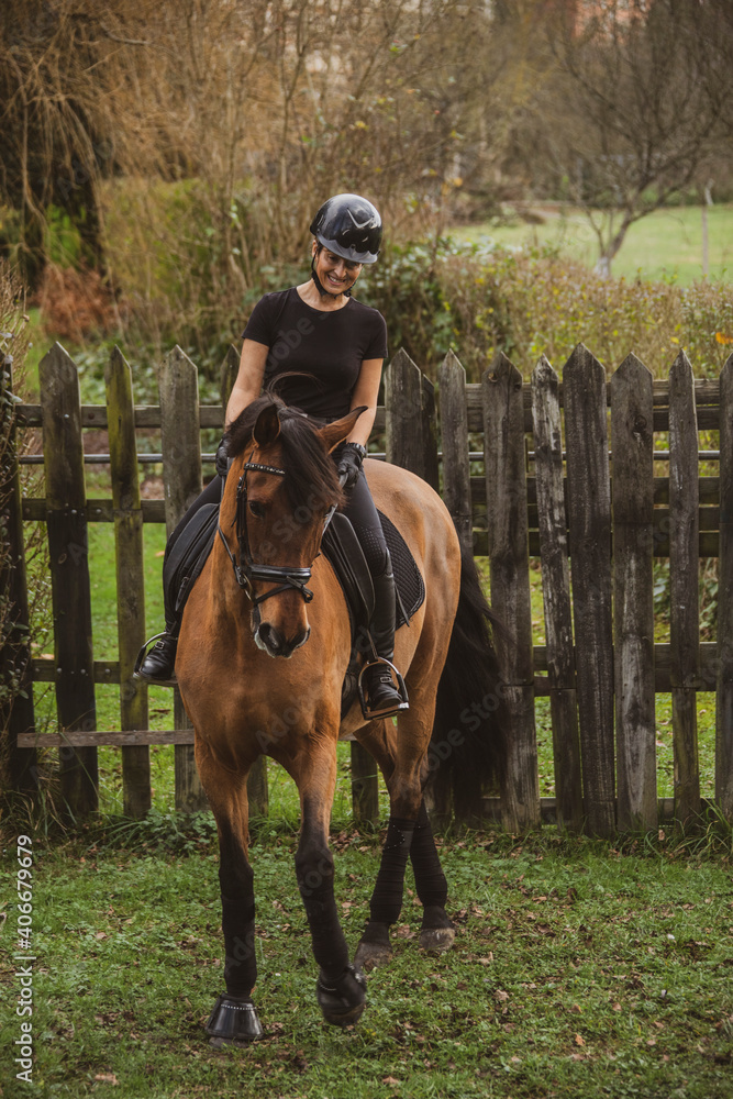 woman riding her brown horse with black mane dressed in black with a helmet woman riding her brown horse with black mane dressed in black with a helmet