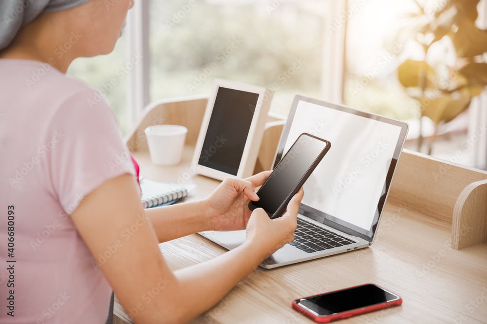 Fototapeta premium Young Asian woman wearing a hijab uses smartphone and laptop at her desk. Attaching a pink ribbon represents recovery from a breast cancer patient. Breast cancer concept, cancer prevention concept.