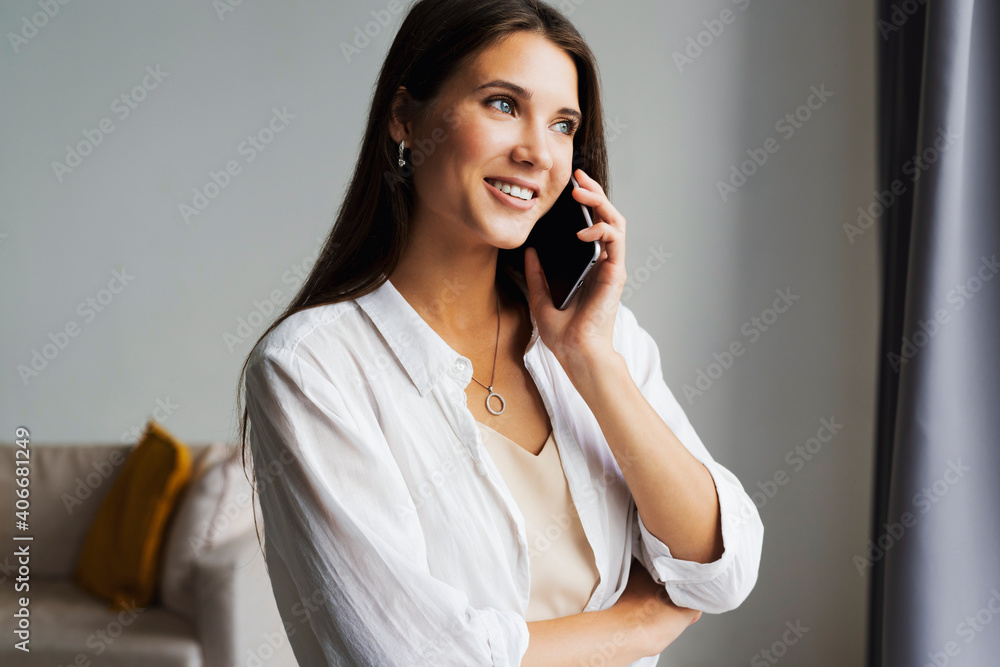 Portrait of business woman, holds smartphone in her hands. Beautiful girl uses mobile phone for work, calls clients, sends text messages. Millennial girl in white shirt stands against white wall Portrait of business woman, holds smartphone in her hands. Beautiful girl uses mobile phone for work, calls clients, sends text messages. Millennial girl in white shirt stands against white wall