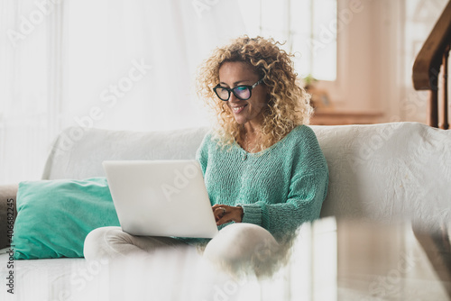 one happy curly woman sitting on the sofa of her home using the computer pc surfing the net - beautiful lady using laptop on the couch of her house
