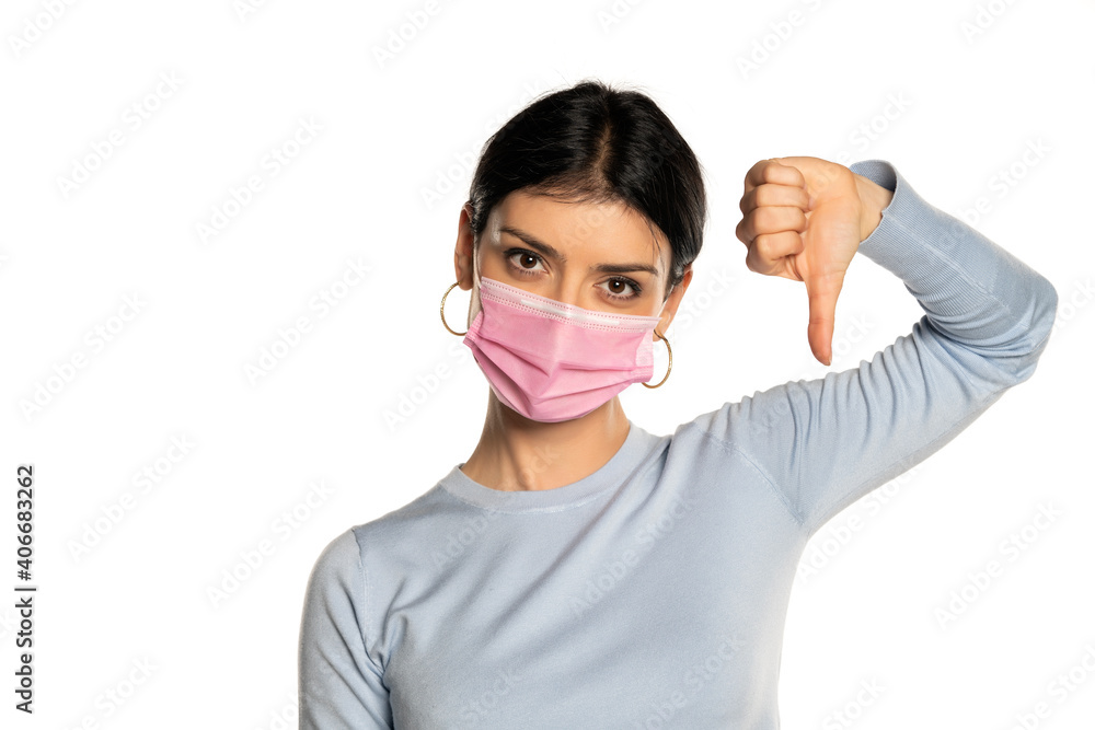Woman wearing a mask and showing thumb down, isolated on white. 