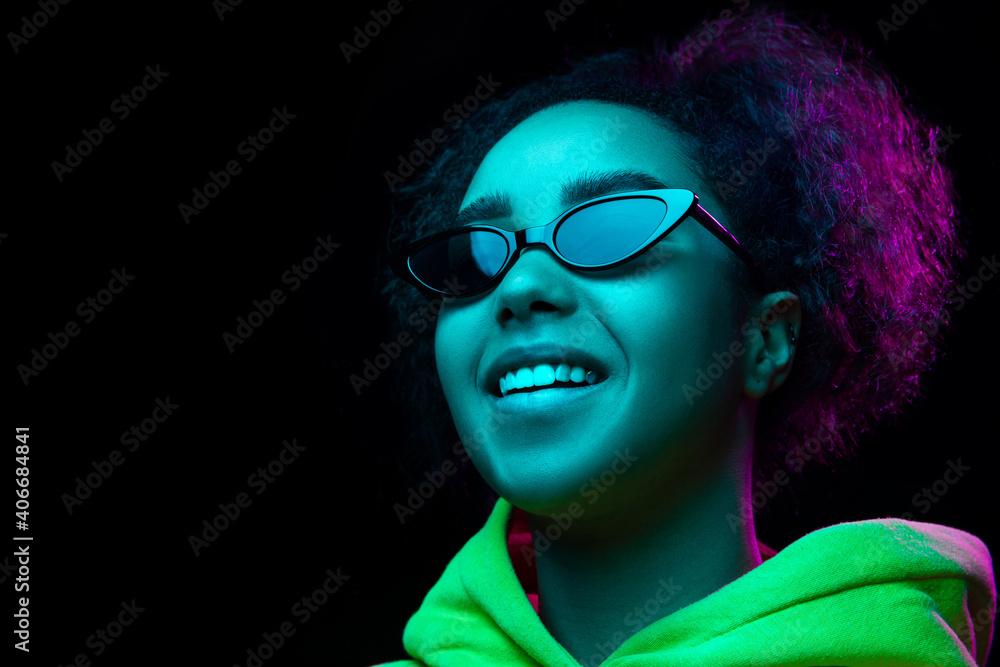 Eyewear. African-american woman's portrait isolated on dark studio background in multicolored neon light. Beautiful female model. Concept of human emotions, facial expression, sales, ad, fashion.