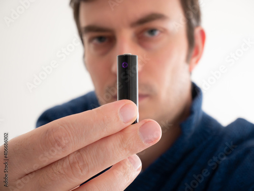 Unbranded AA type black battery held in hand by defocused Caucasian man close up shot shallow depth of field