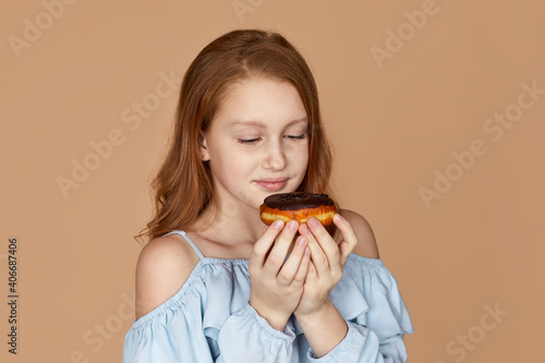 cute child girl tastes yummy chocolate donut isolated on studio background