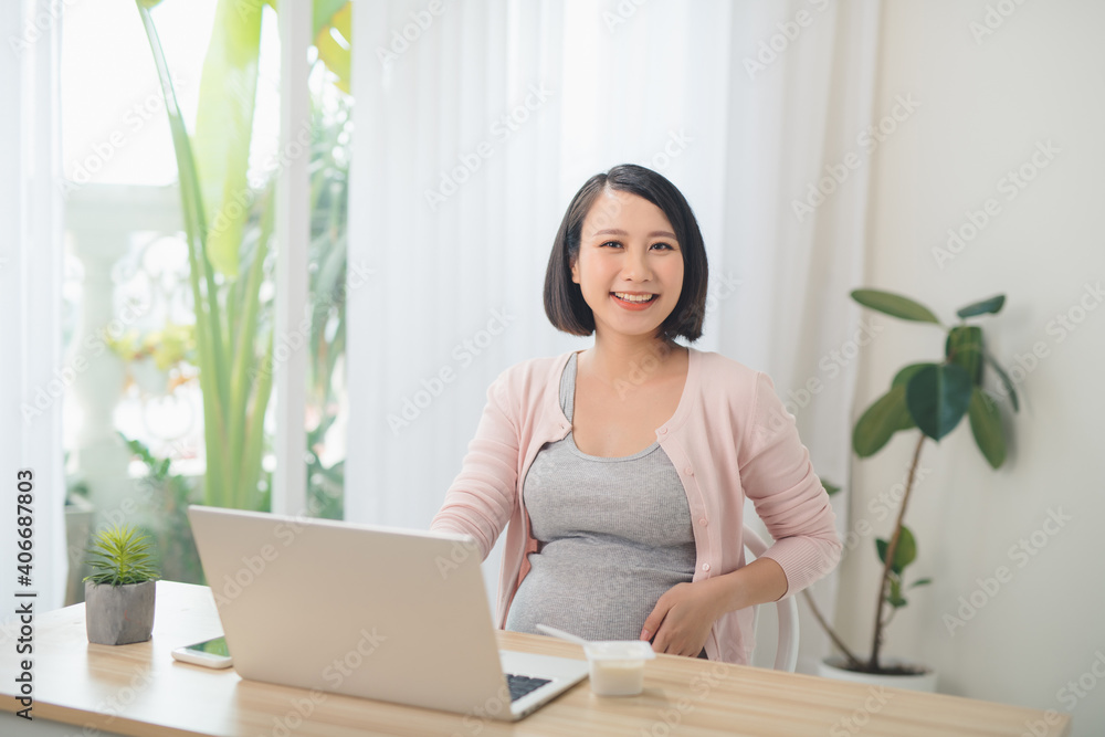 Beautiful pregnant business woman is eating yogurt and smiling while sitting at her working place at home Beautiful pregnant business woman is eating yogurt and smiling while sitting at her working place at home