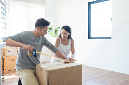 Happy young Asian couple packing box together for moving new house. Young couple.