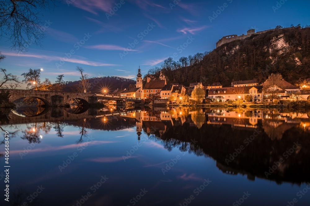 Bild einer Panorama Stadtansicht des Markt Kallmünz Kallmuenz zur blauen Stunde während Sonnenuntergang in Bayern und dem Fluss Naab Vils und der Burg Ruine auf dem Berg, Deutschland