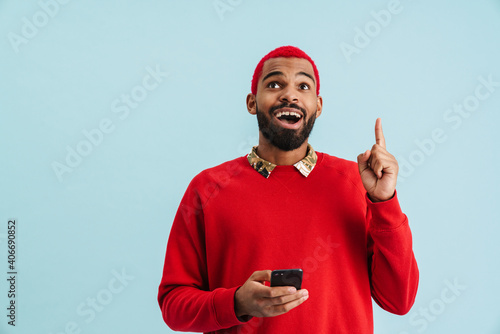 Excited african american guy pointing finger upward while using cellphone