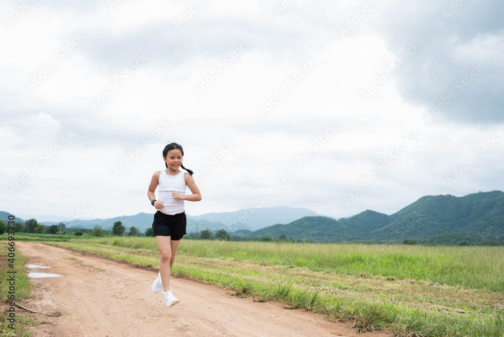 Happy Funny little asian girl fitness woman running at morning tropical forest trail. Athletic young child running in the nature. Healthy lifestyle.