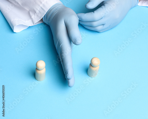 two wooden figures of men stand against the background of the male hands of the doctor in blue latex gloves