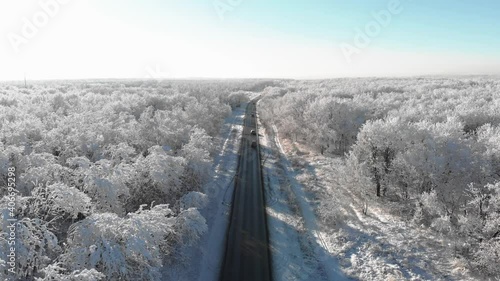 Video from the copter. View to the srerhu. A road with passing cars in the middle of a snowy forest. White snowy trees. Flight over the winter road. 4k. Russia, winter. photo