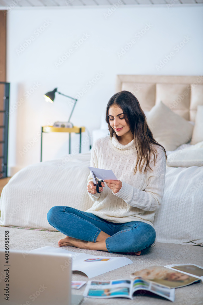 Dark-haired young woman cutting pistures from magazines and making a wishlist Dark-haired young woman cutting pistures from magazines and making a wishlist