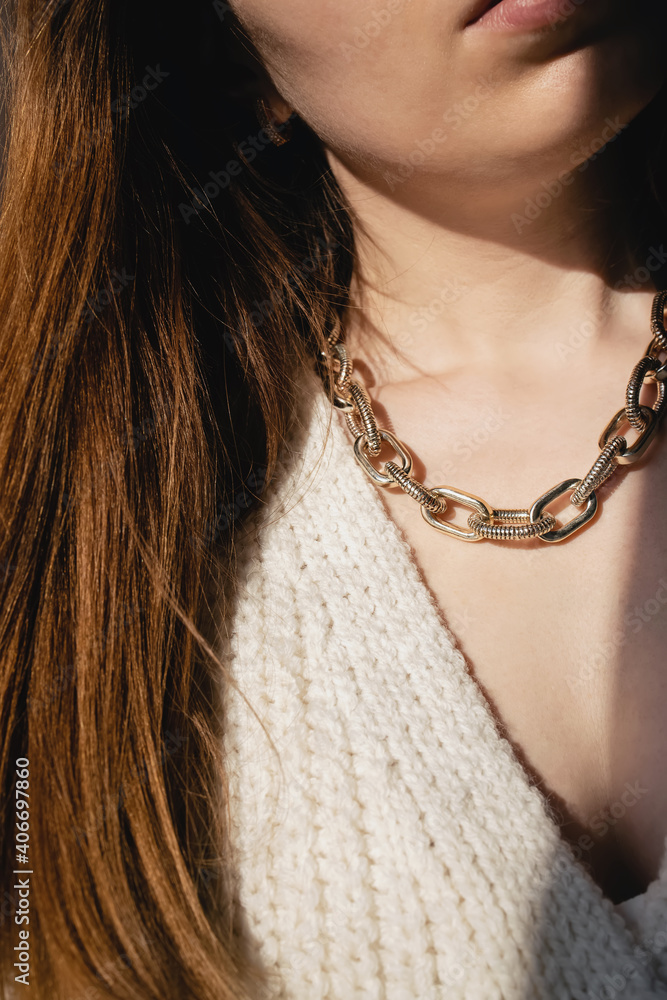 Close-up young woman in white sweater wearing golden chain necklace.