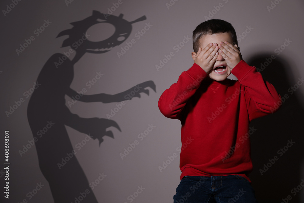Shadow of monster and scared little boy on beige background