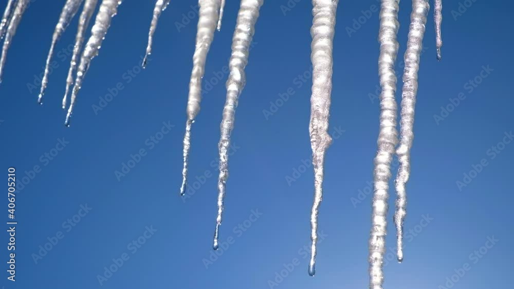 Melting icicles hanging down from roof with blue sky background. Sunny day. Spring, warming concept. Warm winter day. Falling down icicles danger concept. Melting icicles hanging down from roof with blue sky background. Sunny day. Spring, warming concept. Warm winter day. Falling down icicles danger concept.