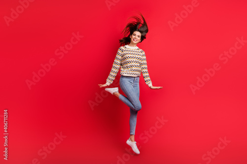 Full length body size photo of childish careless girl jumping with blowing hair smiling isolated bright red color background